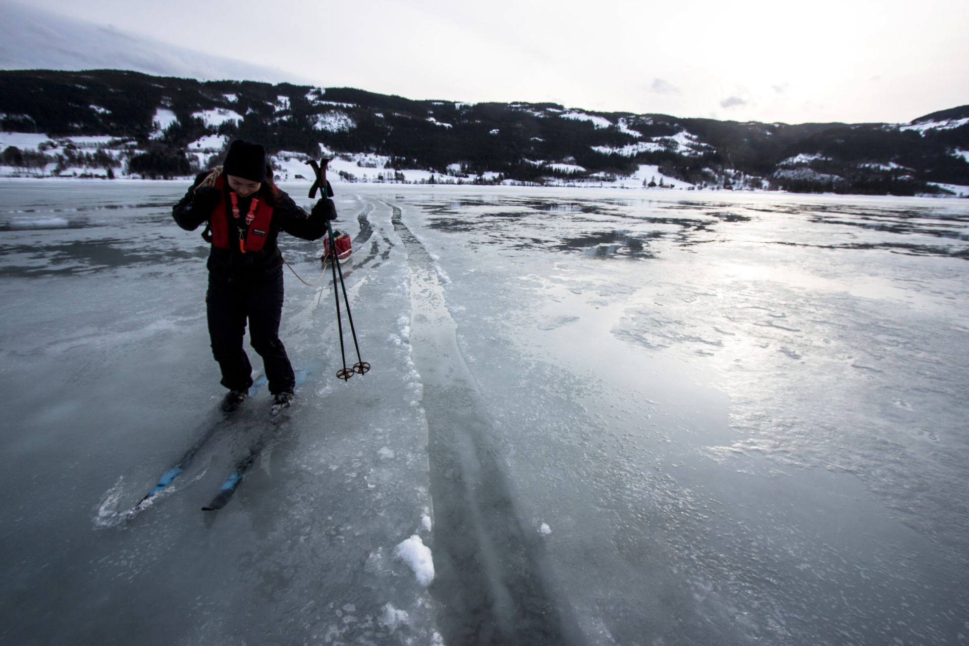 Mye overvann på et vann og en skiløper som står i det.