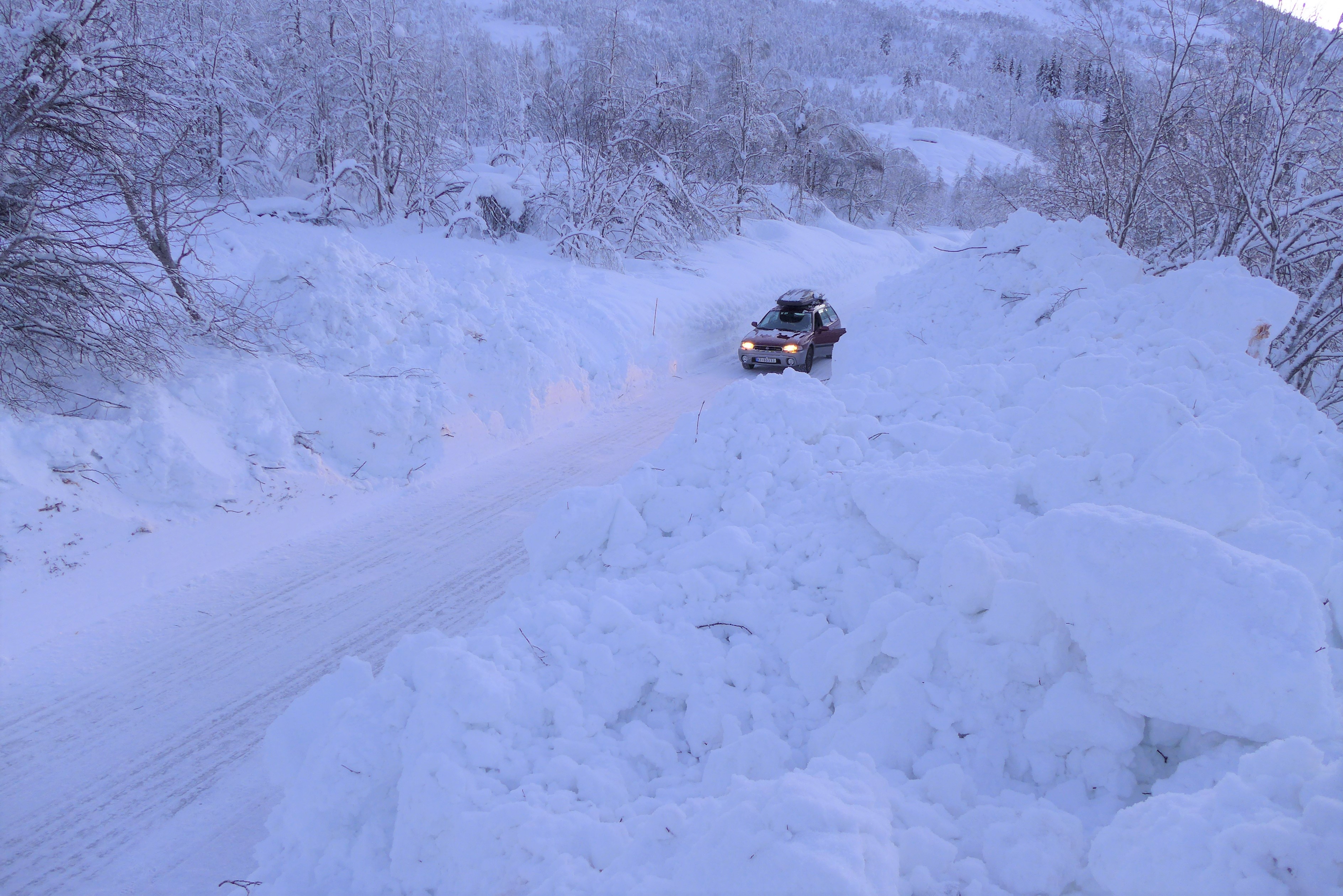 En bil som står parkert på en vei hvor det har gått et snøskred over.
