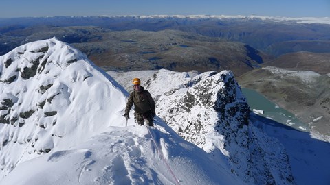 En person på tur med stegjern og isøks på vinterdekt fjell.