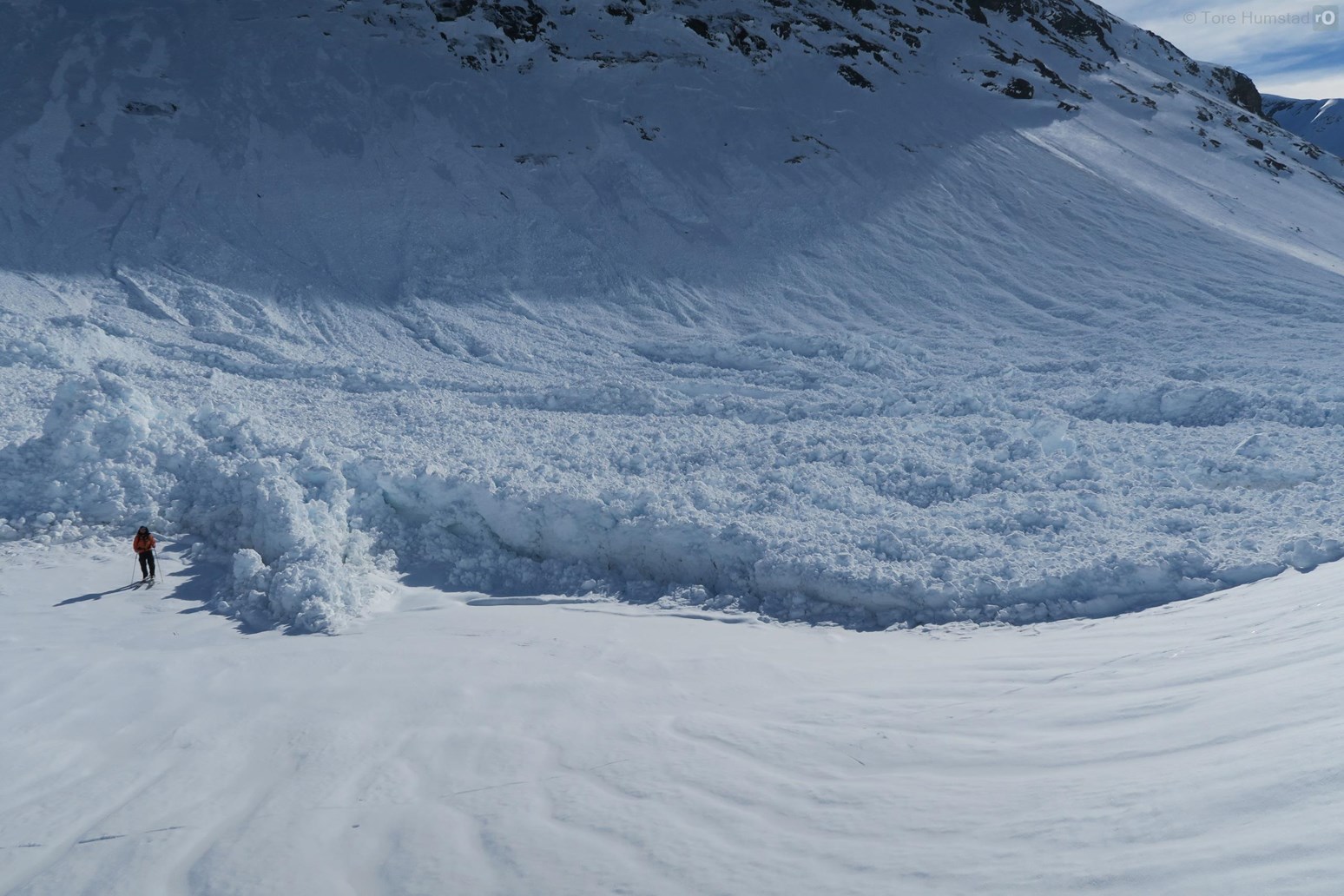 En skigåere står ved siden av skredavsetningene til et svært stort vått flakskred.